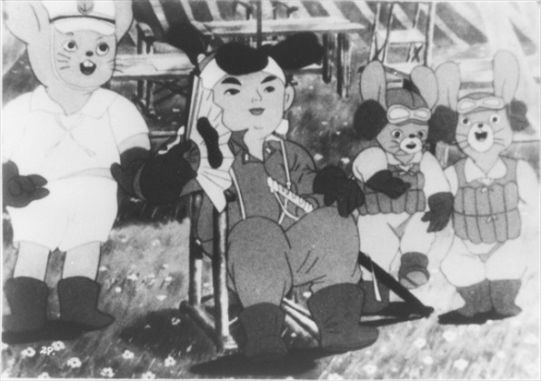 A black and white cartoon image. A boy in a flight suit, wearing a hachimaki and holding a fan with the Rising Sun on it, sits in a deckchair. Beside him stand three excited anthropomorphic rabbits, dressed in Japanese WW2 military uniforms.