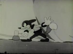 A black and white cartoon image. In front of a canvas background, an anthropomorphic fox is grimacing, as he hits a rock with a hammer.